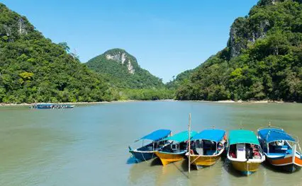 A group of boats docked on a river near a mountain.